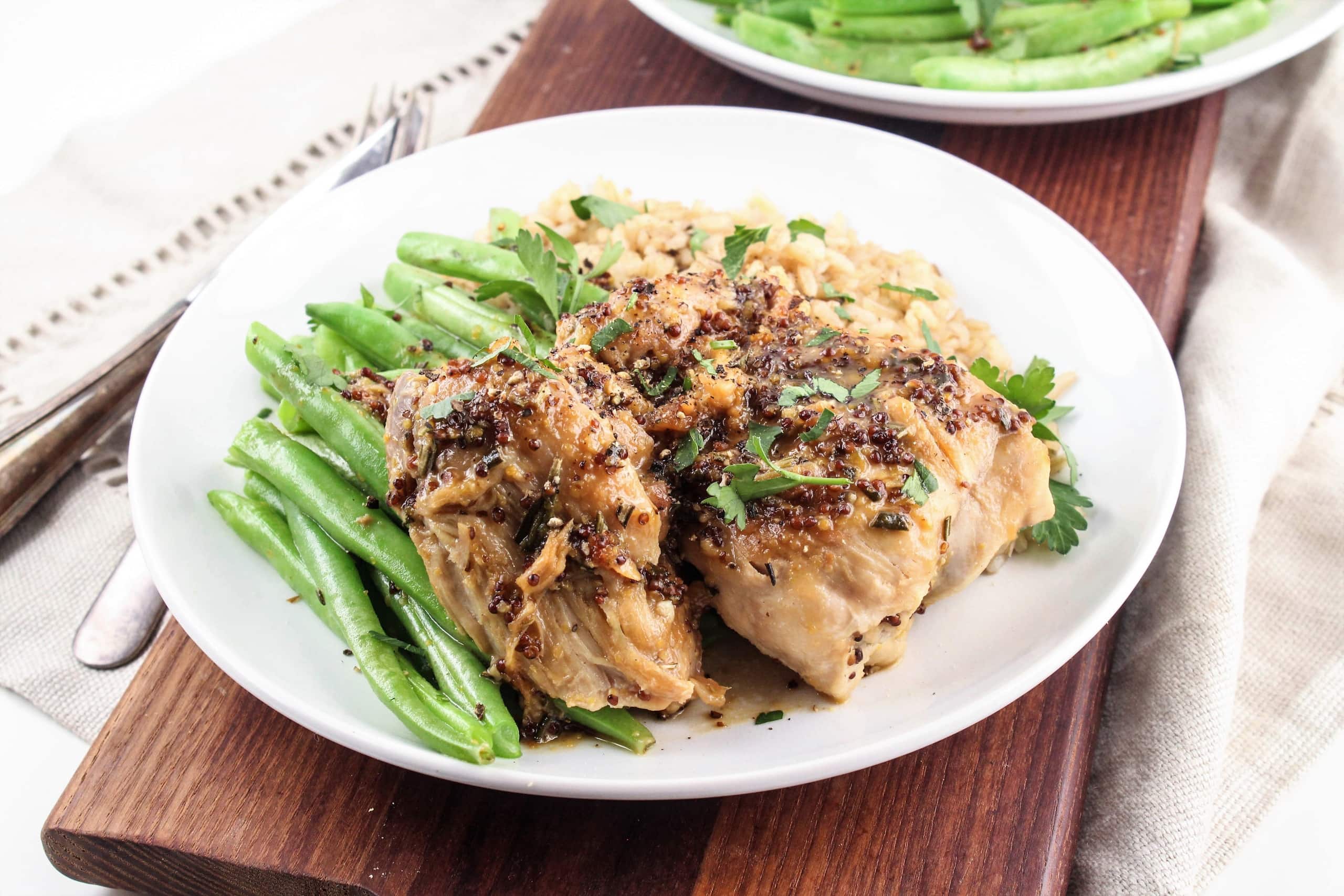Two chicken thighs with maple mustard sauce on top next to green beans on a white plate.