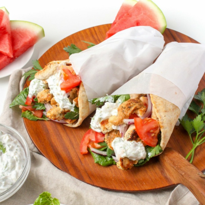 grilled chicken gyro wraps on a wooden platter next to a glass bowl with tzatziki sauce