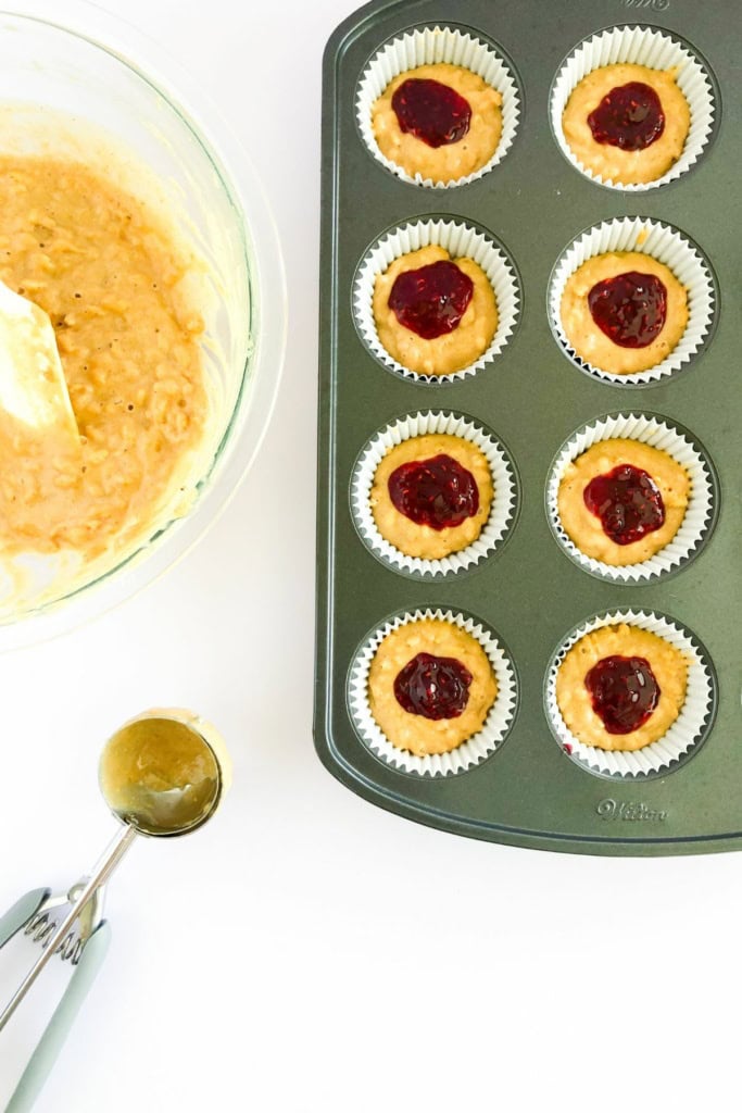 peanut butter muffin batter in a muffin tin with jelly