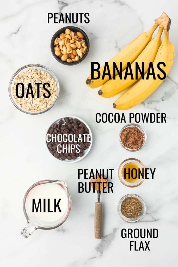 bananas, oats, chocolate chips, peanut butter, and milk on a white marble background