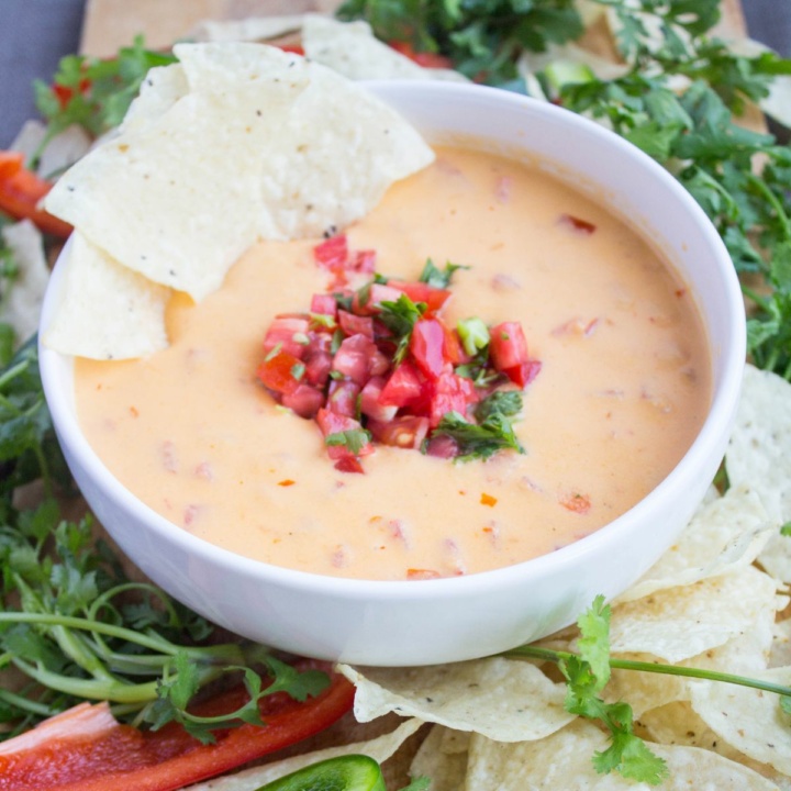 spicy hummus queso in a white bowl with diced tomatoes and tortilla chips