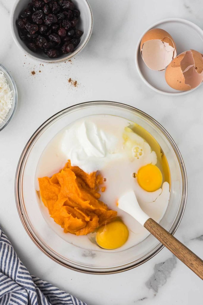 eggs, Greek yogurt, sweet potato puree, and almond milk in a glass bowl with a white spatula