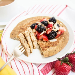 a large banana egg pancake on a white plate topped with berries and sliced almonds