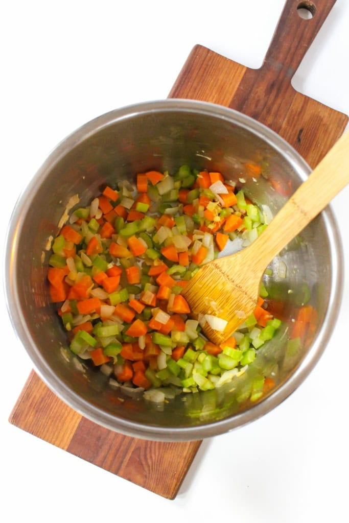 diced carrots, celery, and onions in an Instant Pot with a wooden spoon