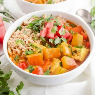 tofu curry in a bowl with watermelon rind chunks, brown rice, and fresh herbs