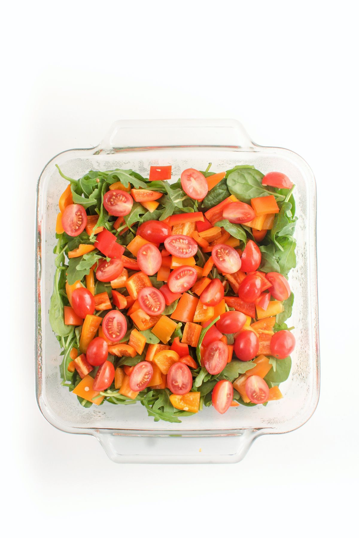 square glass baking dish filled with cherry tomatoes, spinach, and orange bell peppers