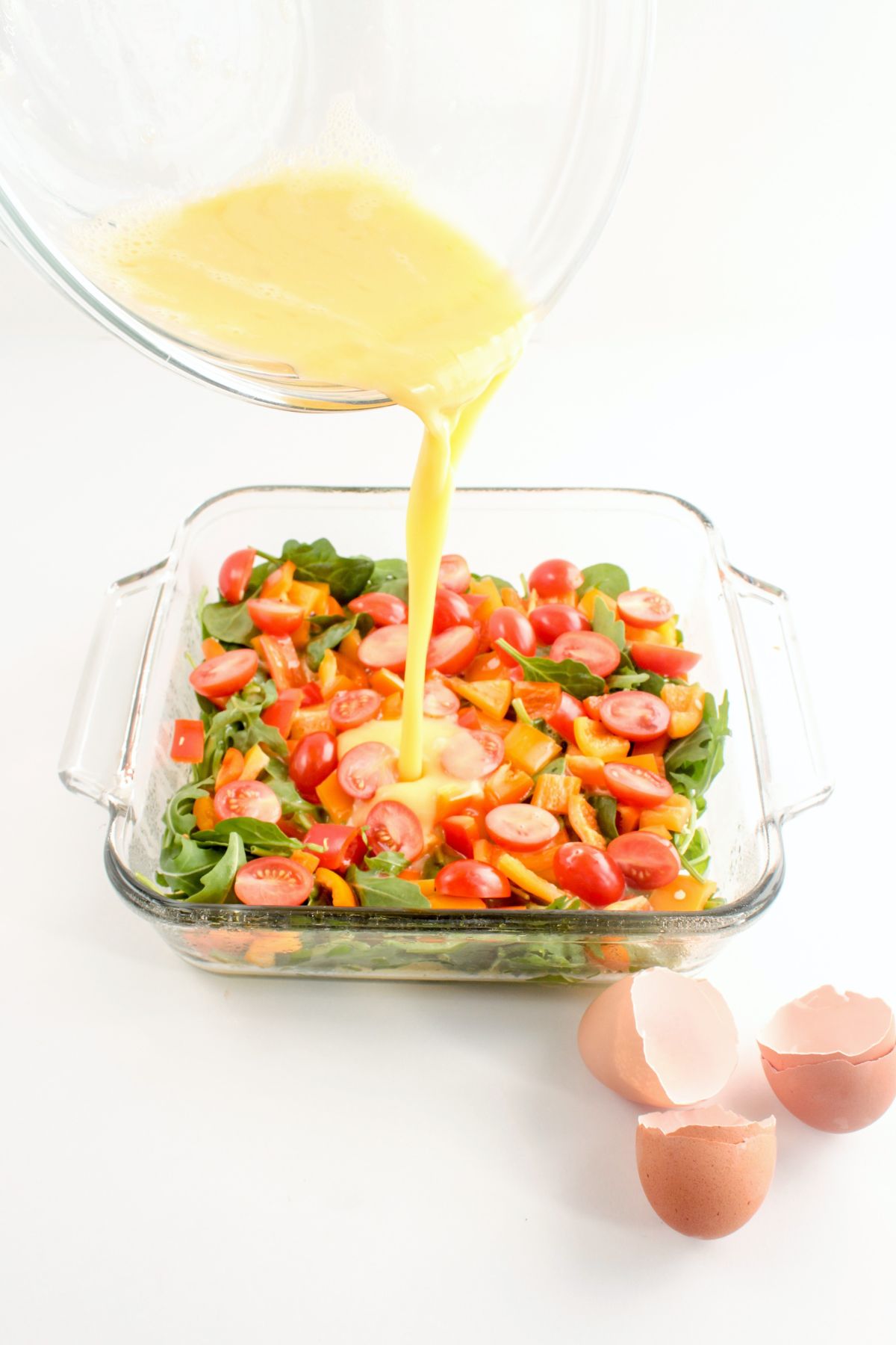 raw scrambled eggs being poured into a glass baking dish with vegetables in it 