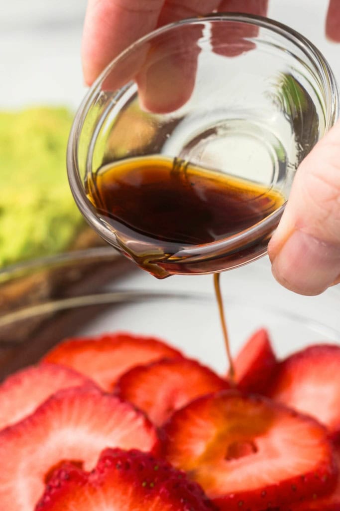 balsamic vinegar being poured over a bowl of sliced strawberries
