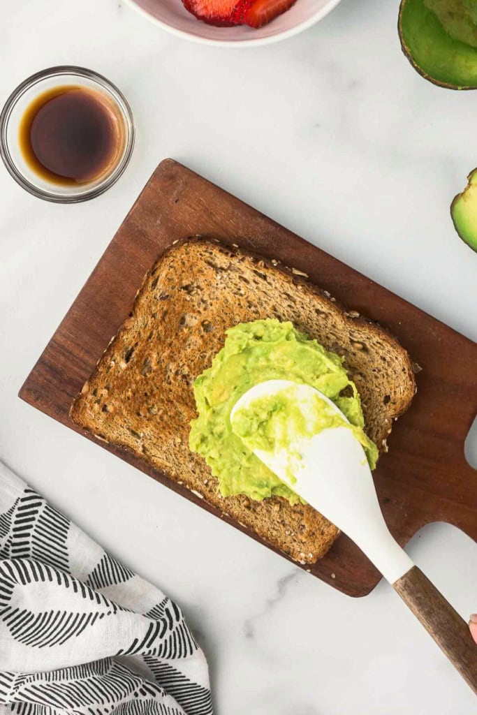 mashed avocado being spread over toast with a white spatula