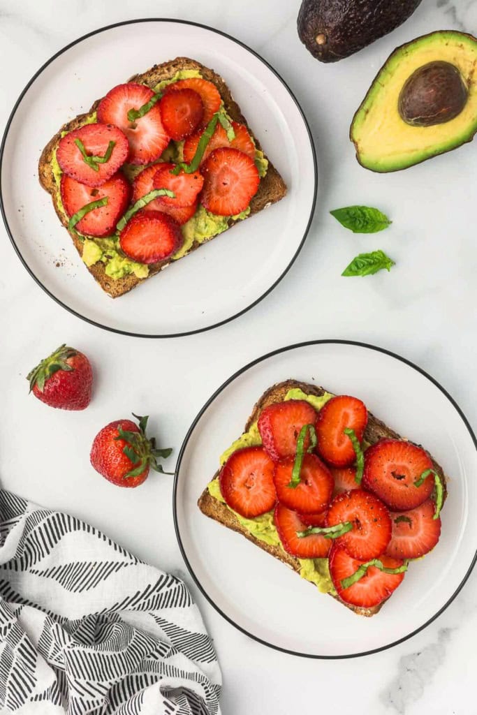 two slices of toast with sliced strawberries and avocado on top