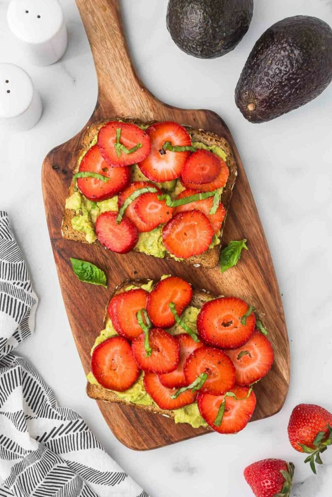 two slices of strawberry avocado toast with balsamic on a wooden platter