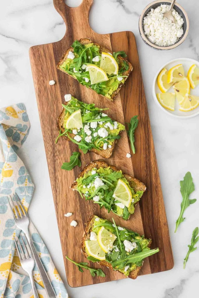 goat cheese avocado toast on wooden platter with lemon slices
