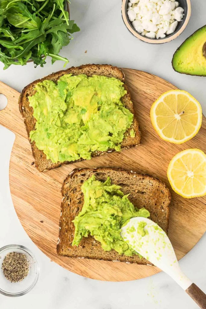two slices of toast with mashed avocado on a wooden platter