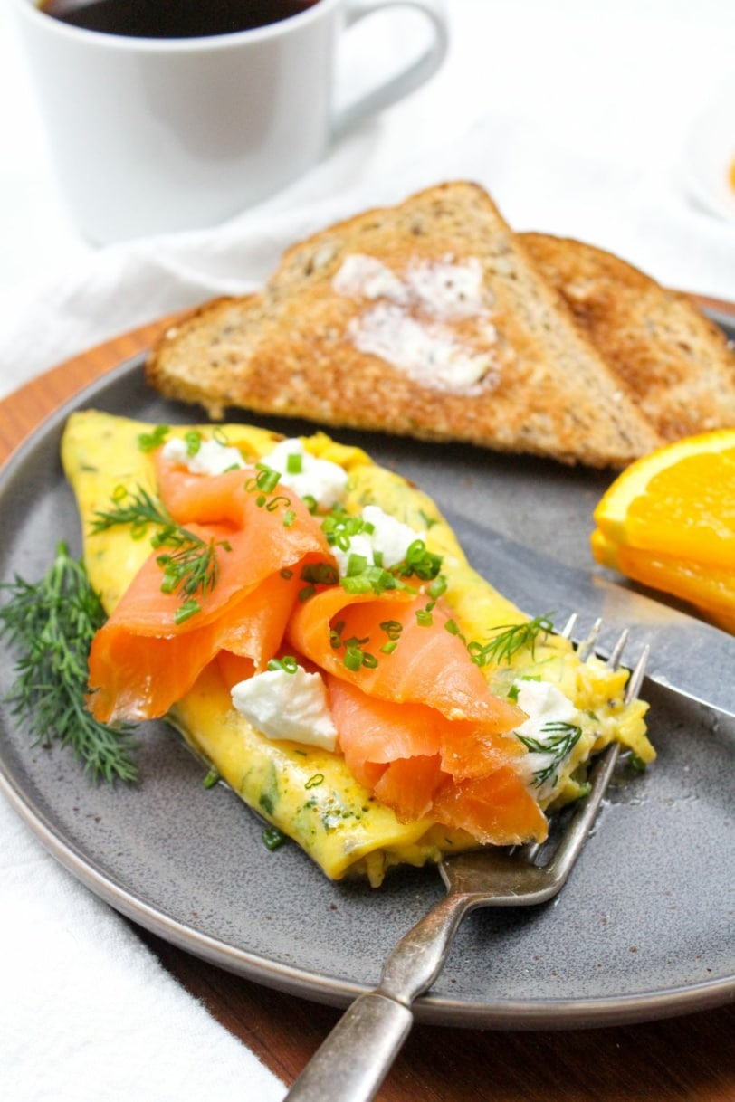 smoked salmon omelette with goat cheese and herbs on a plate with a mug of coffee and toast