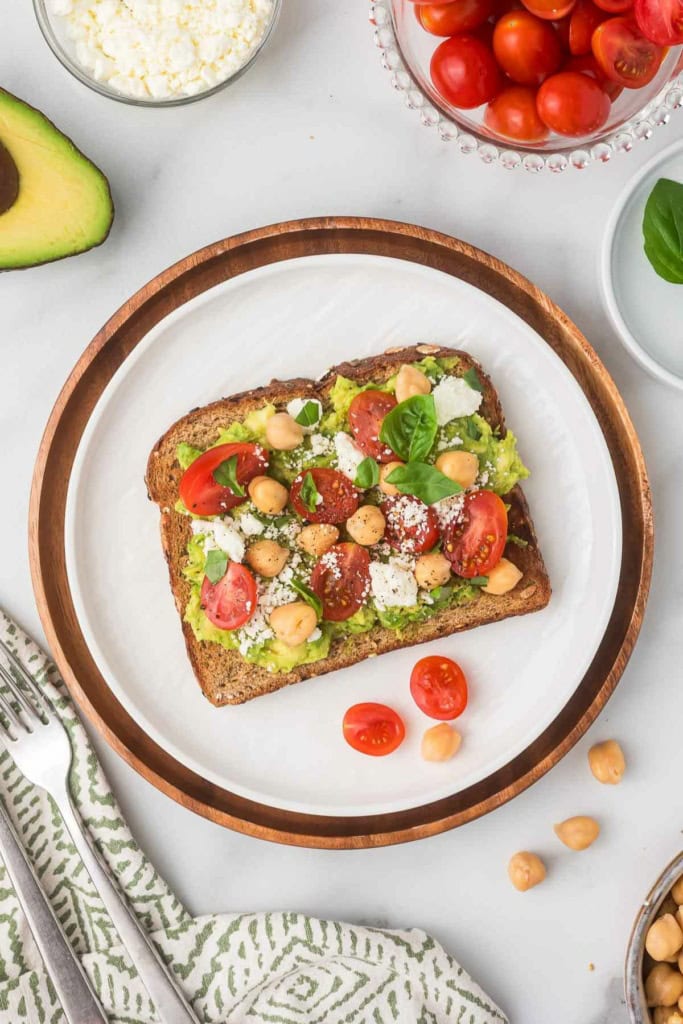 a slice of Mediterranean avocado toast with feta on a white plate