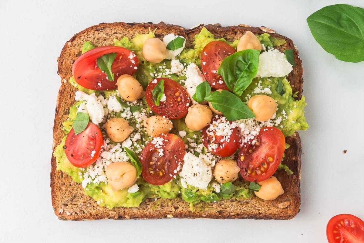 a slice of Mediterranean feta toast with avocado, tomatoes, and chickpeas on top