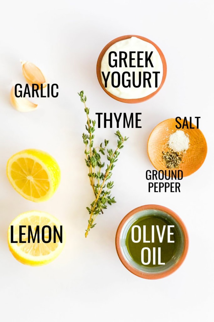 lemons, Greek yogurt, garlic cloves, olive oil, and thyme sprigs on a white background