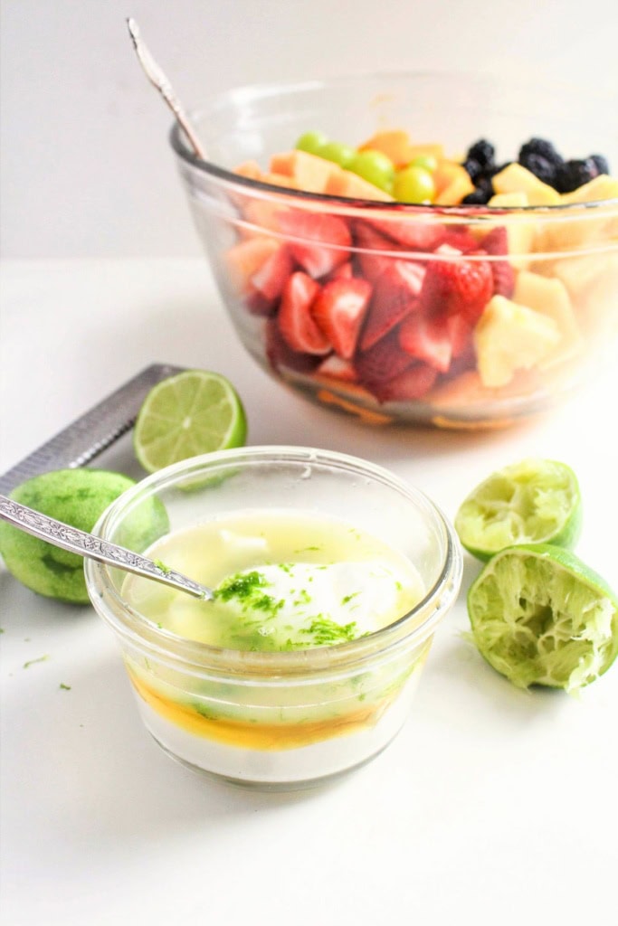 Greek yogurt with honey and lime in a small glass bowl next to a bowl of fruit