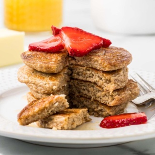 stack of fluffy cottage cheese pancakes topped with sliced strawberries and maple syrup on a white plate