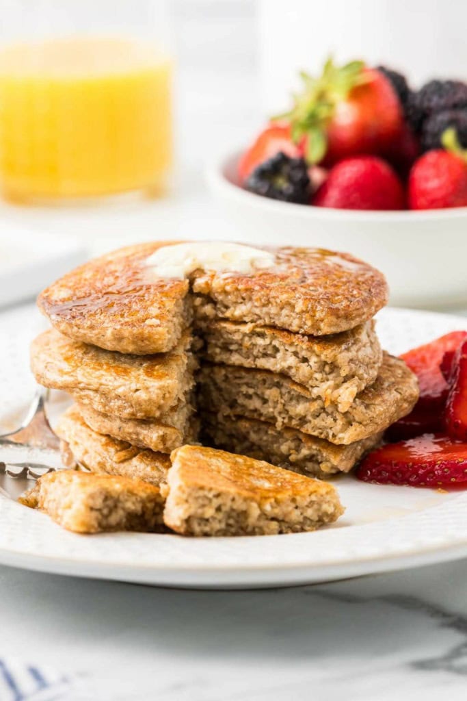 stack of cottage cheese pancakes with a bite cut out on a fork and a bowl of mixed berries behind it