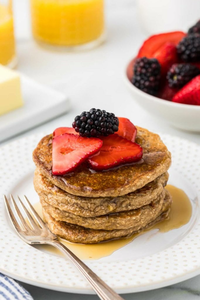 protein pancakes with sliced strawberries and blackberries on top with a glass of orange juice in the background