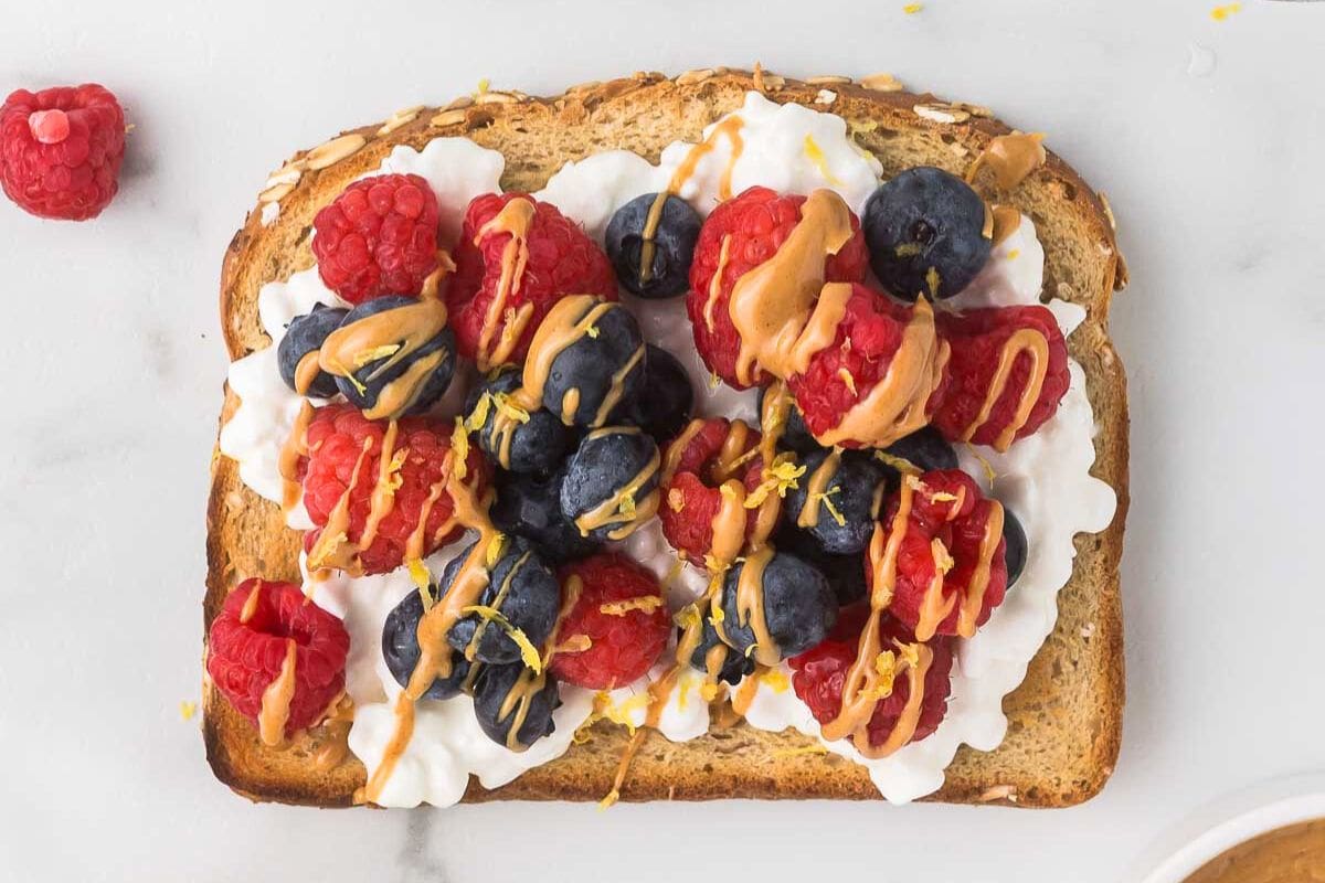 a slice of toast topped with cottage cheese, berries, and nut butter