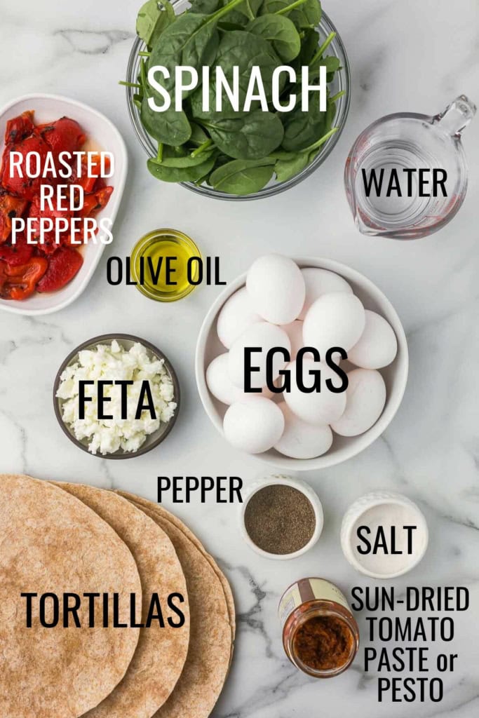 eggs, tortillas, spinach, sun-dried tomato paste, roasted red peppers, and feta cheese on a marble countertop