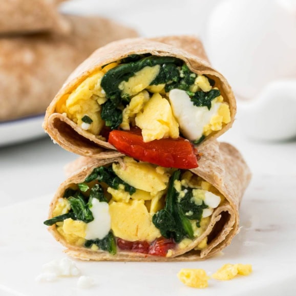 spinach feta wrap with eggs cut in half and stacked on a white marble background