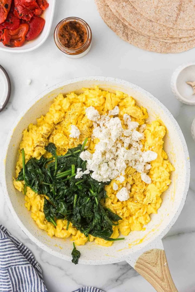 scrambled eggs, feta cheese, and spinach in a white skillet