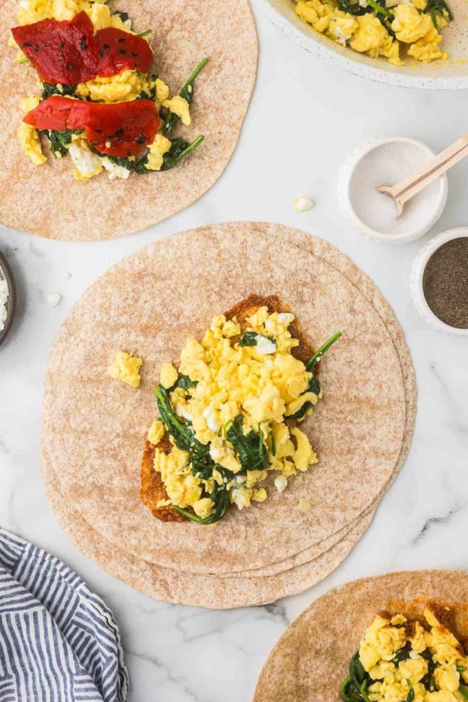 scrambled eggs, feta cheese, and spinach on a whole wheat tortilla