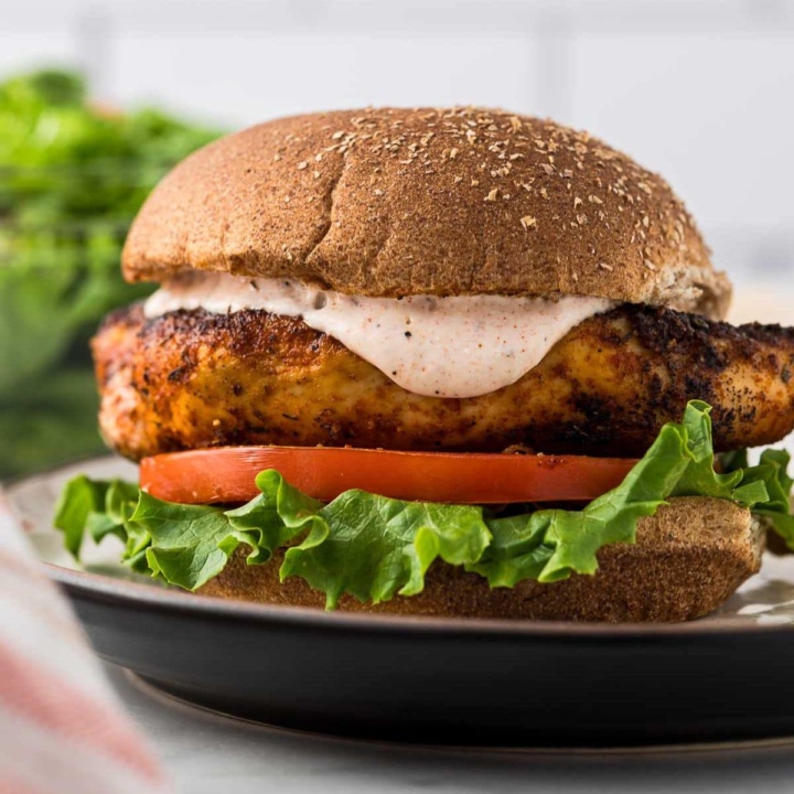 blackened chicken sandwich with chipotle yogurt sauce, lettuce, and tomato on a plate