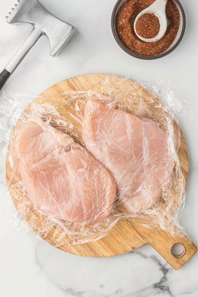 raw chicken breasts next to a meat mallet