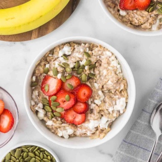 cottage cheese oatmeal in a white bowl topped with sliced strawberries and pumpkin seeds