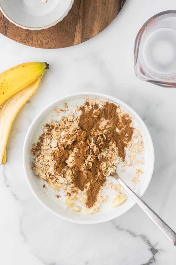 a white bowl with oats, cinnamon, mashed banana, and milk mixed together