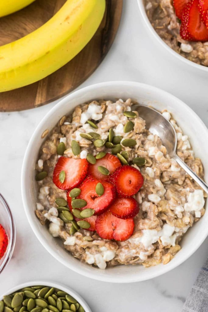 a bowl of cottage cheese oatmeal with sliced strawberries and pepitas