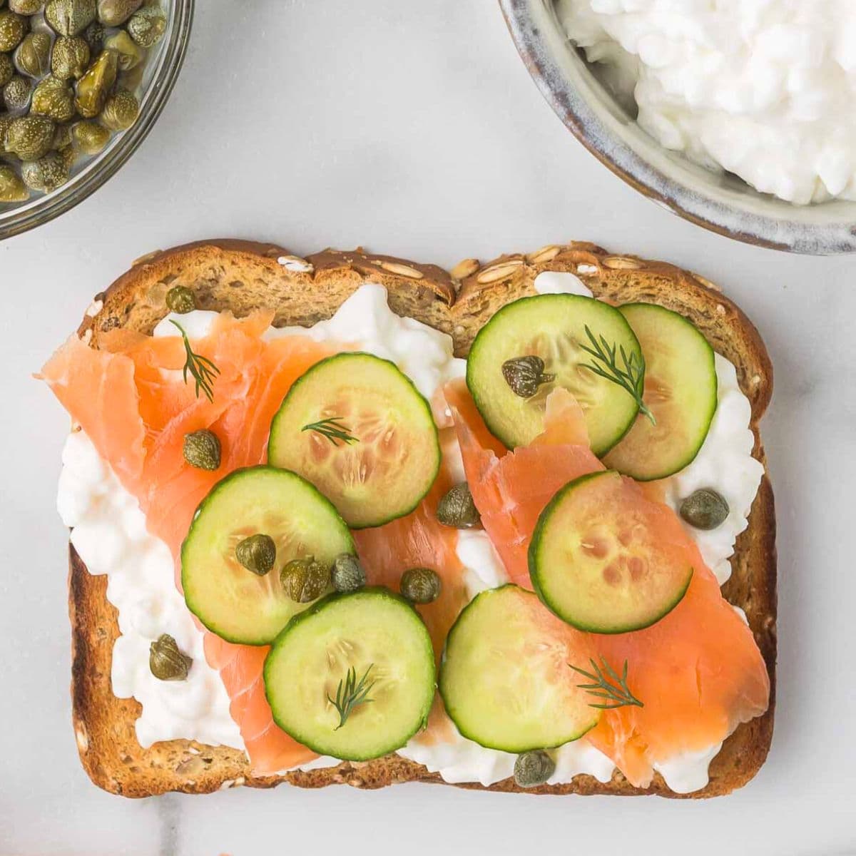 cottage cheese toast with smoked salmon and cucumber on a white marble background